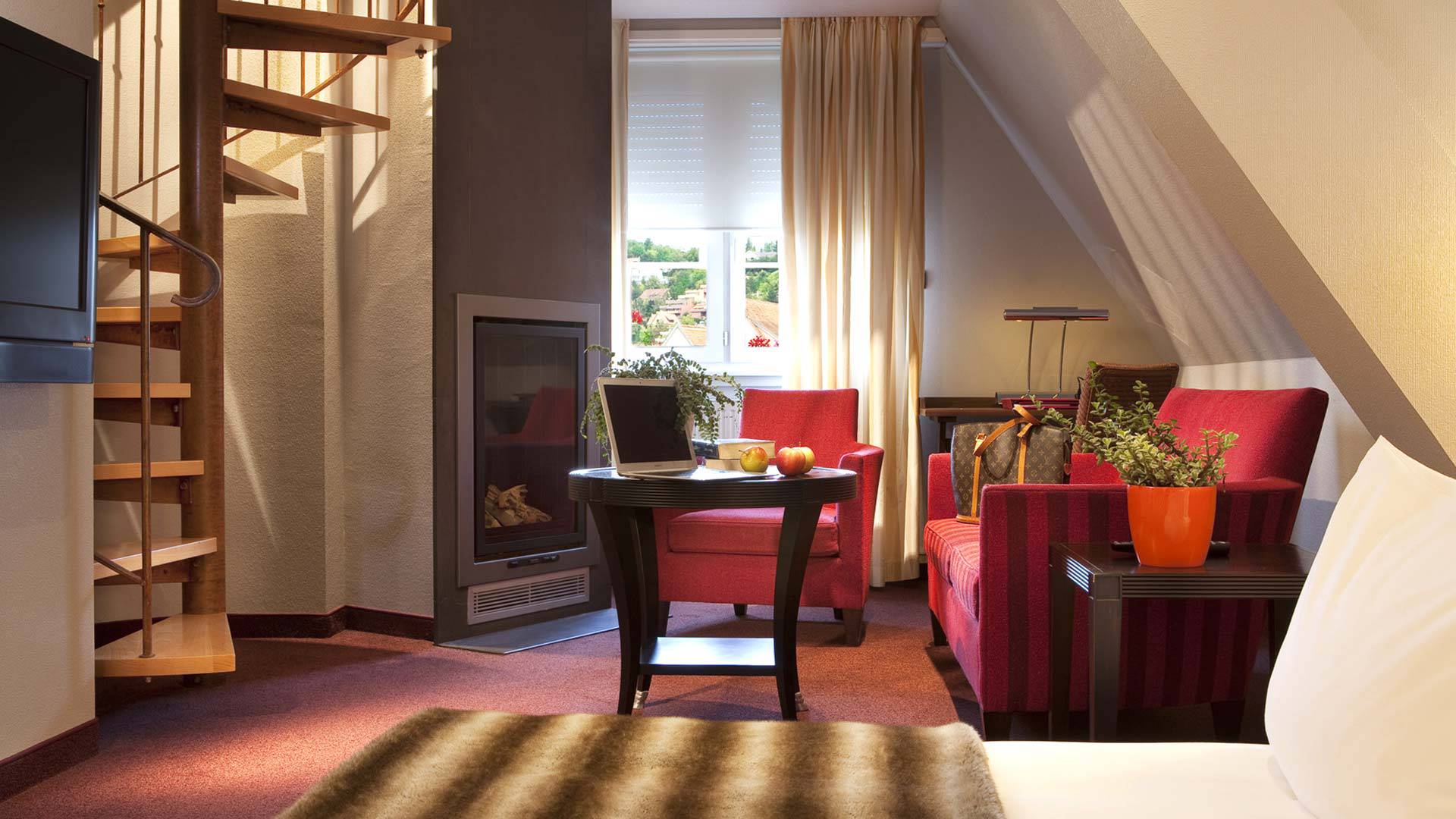 Salon confortable avec fauteuils rouges et escalier en colimaçon - Hôtel de Charme Alsace - Yona Hôtel