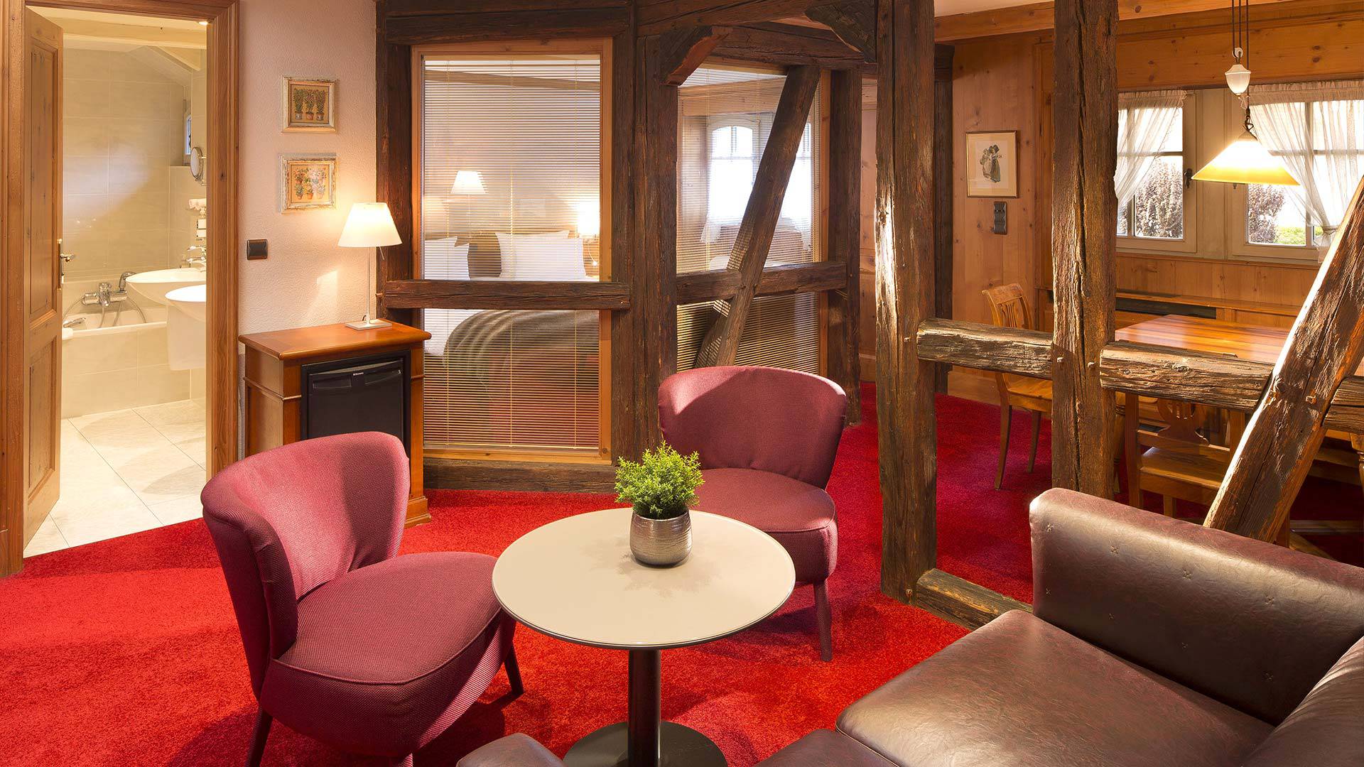 Salon chaleureux avec fauteuils rouges et table.