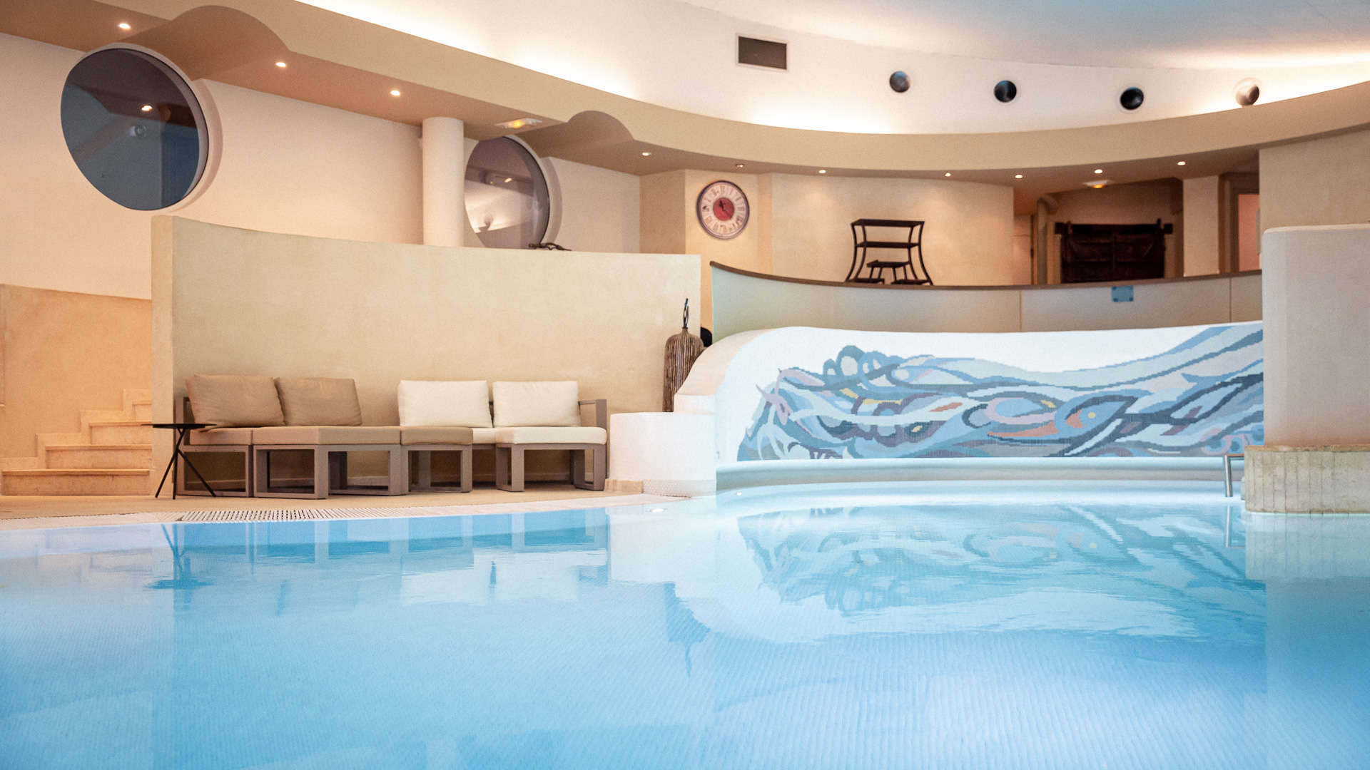 Piscine intérieure luxueuse avec décor mural artistique.