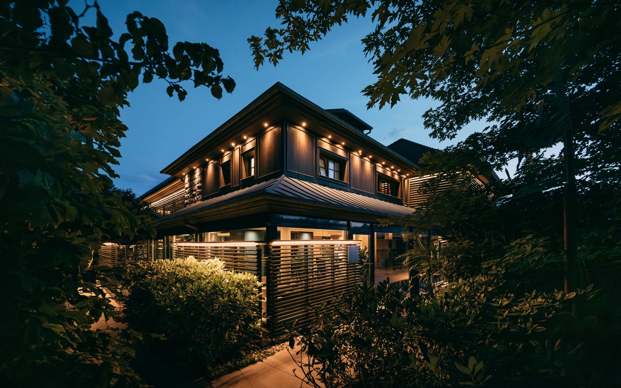 Maison moderne éclairée la nuit, entourée de végétation - Hôtel Spa Alsace