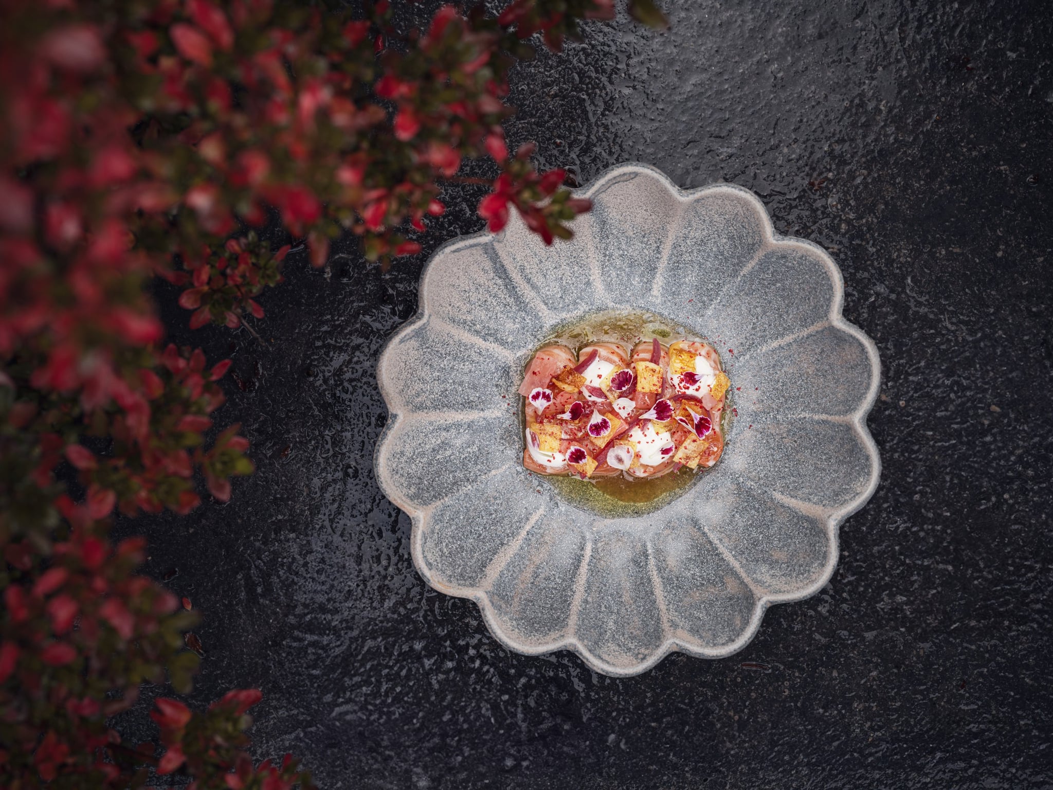 Assiette gourmande sur table noire avec fleurs rouges.