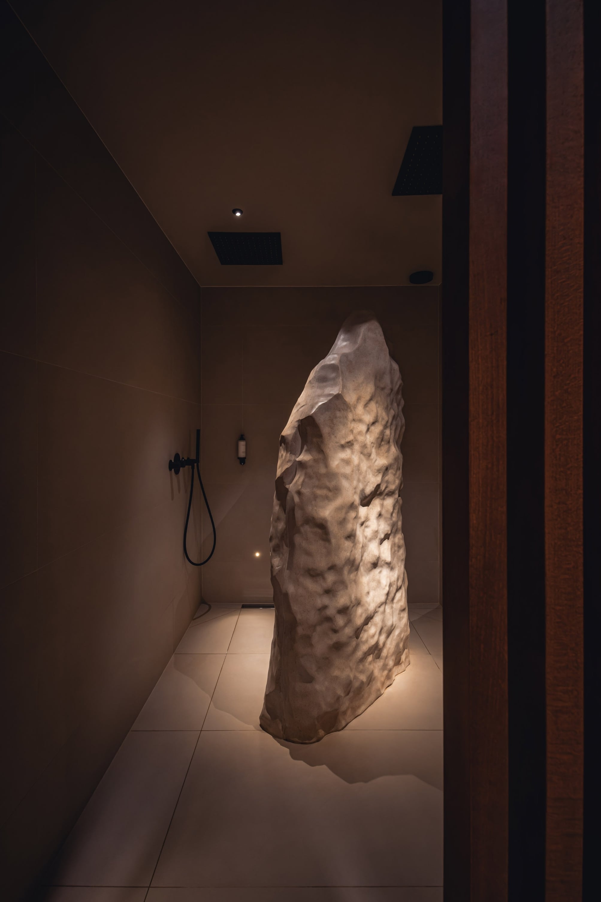 Douche minimaliste éclairée avec une grande pierre centrale.