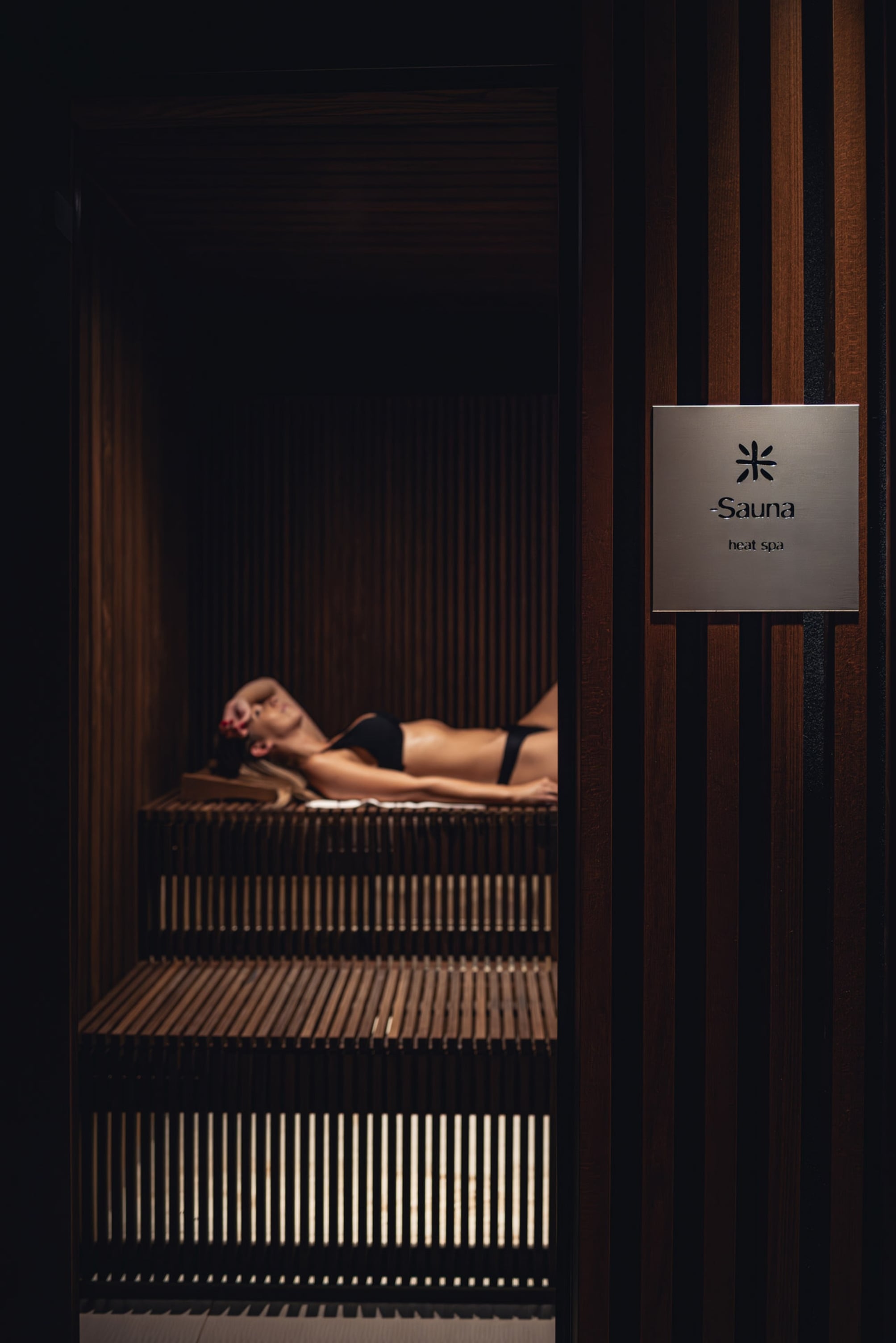 Femme relaxant dans un sauna en bois sombre.