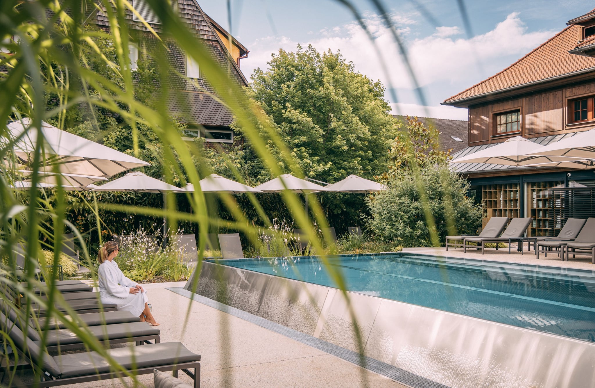 Femme relaxant près d'une piscine extérieure, parasols visibles.