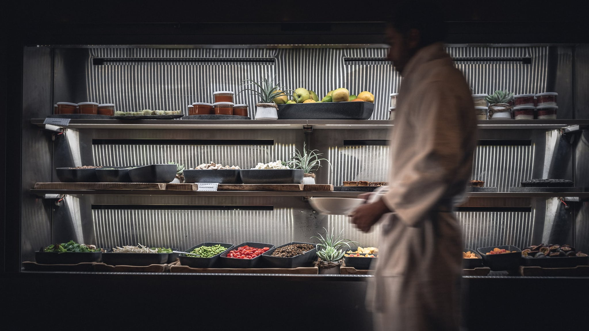 Chef près d'étagères de fruits et plats.