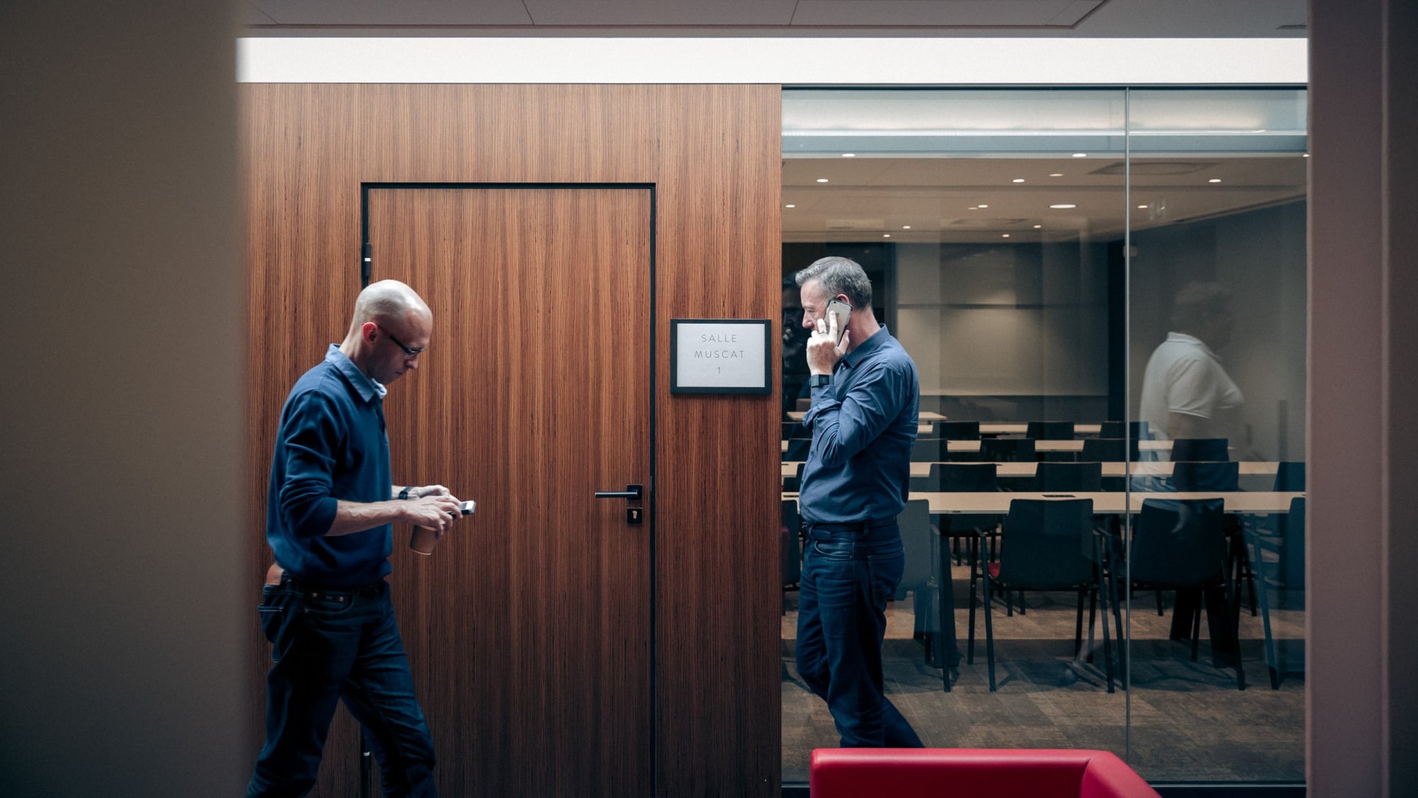 Deux hommes devant la salle Muscat 1, téléphonent.