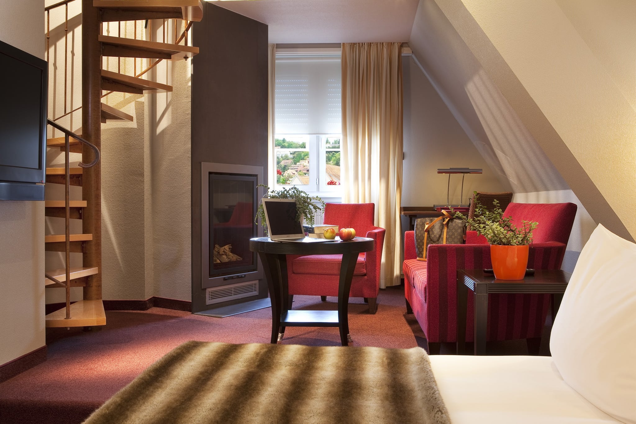 Chambre moderne avec escalier, cheminée et fauteuils rouges.