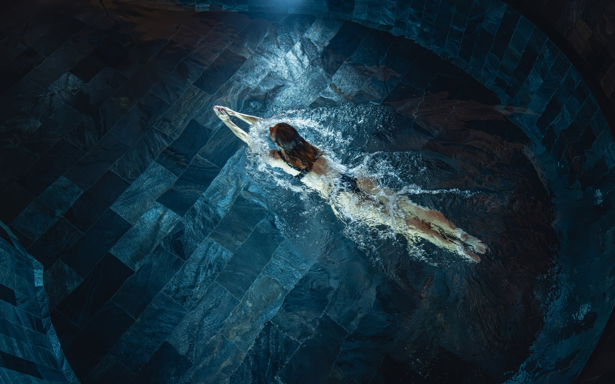Personne nageant dans une piscine sombre.