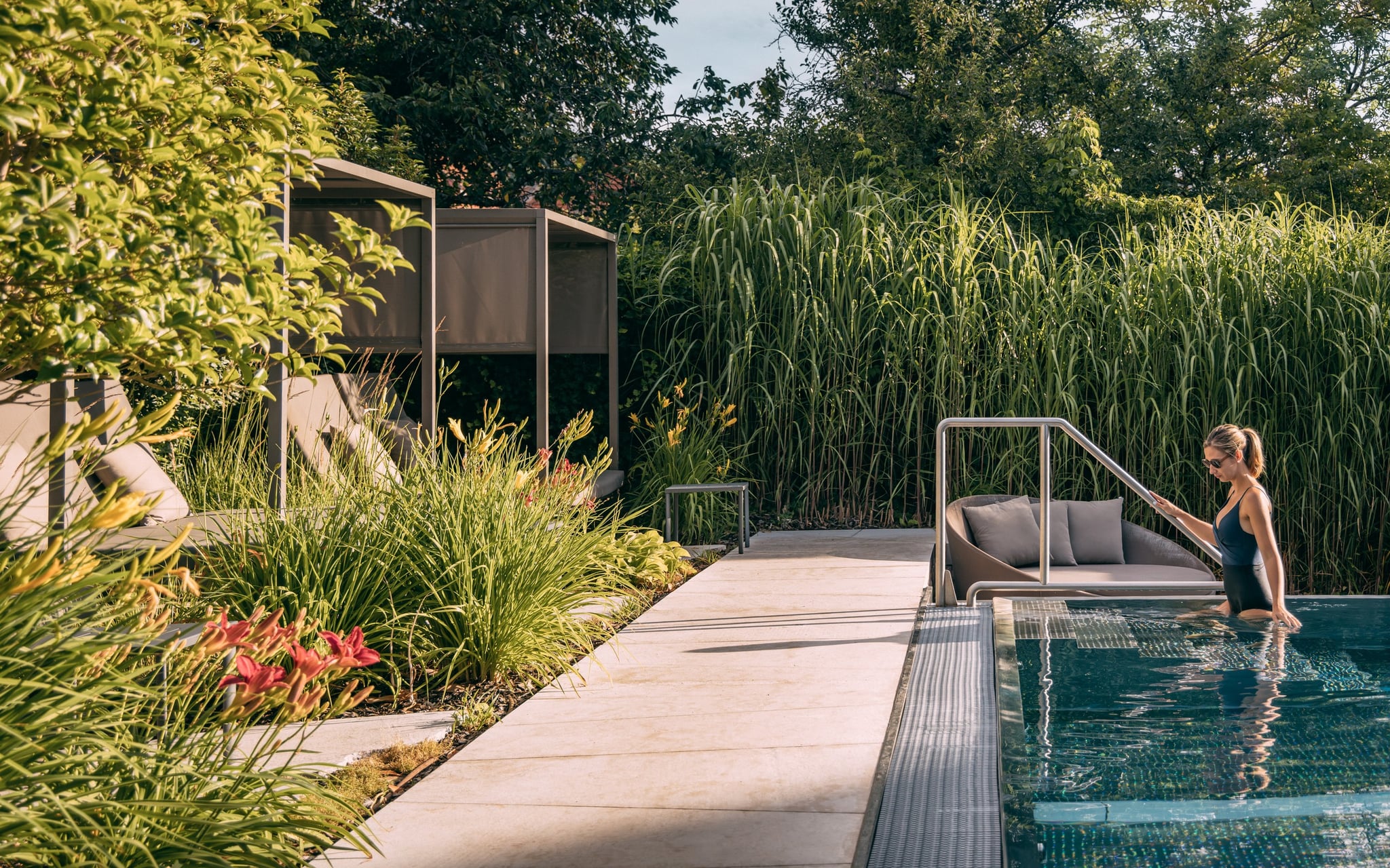 Femme entre dans une piscine moderne entourée de verdure.